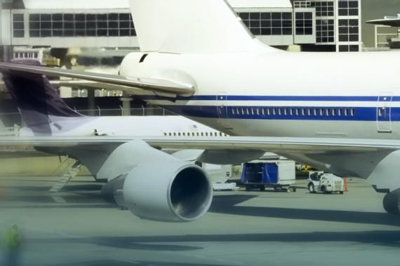 A stock image of an airport apron with two airplanes in the foreground and an airport building in the background