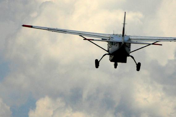 A small plane flying through a cloudy sky seen from behind