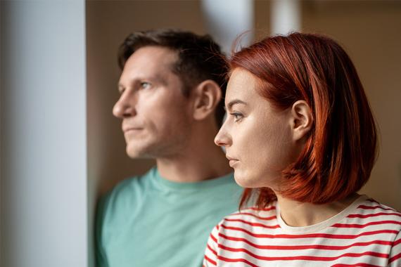 A young man and young woman are looking out a window. They appear to be calmly thinking about something serious