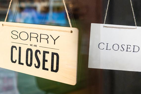 Two "closed" signs hang side-by-side on a glass door. The one on the left says "Sorry we are closed" and the one on the right says "Closed."