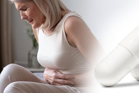 A sitting woman has her hands over her stomach. She is doubled over and in pain. An enlarged picture of a white capsule is beside her image