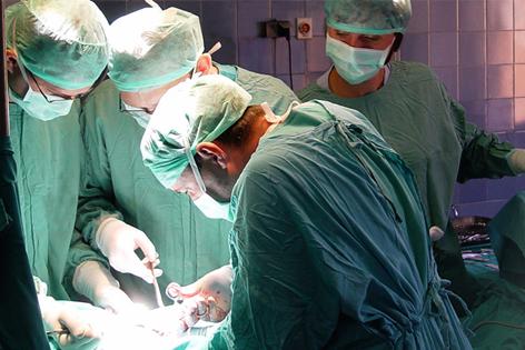 Three surgeons and an assistant in green surgical gowns and masks performing surgery on a patient
