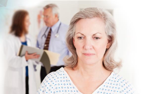 A woman is standing and looking to the side. A doctor and nurse are in a discussion behind her. They are holding an open file folder
