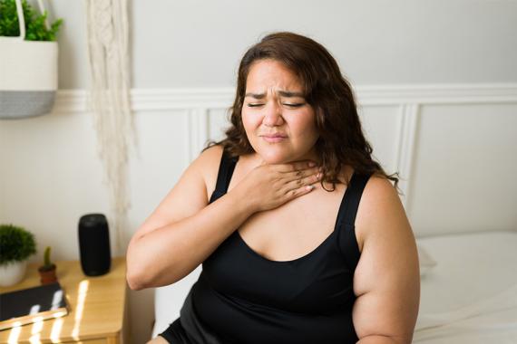 A woman wearing a black tank top holds her throat with a pained expression on her face