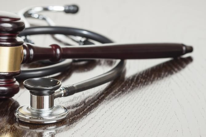 A stock image of a judge's gavel and a stethoscope lying on a wooden desk.
