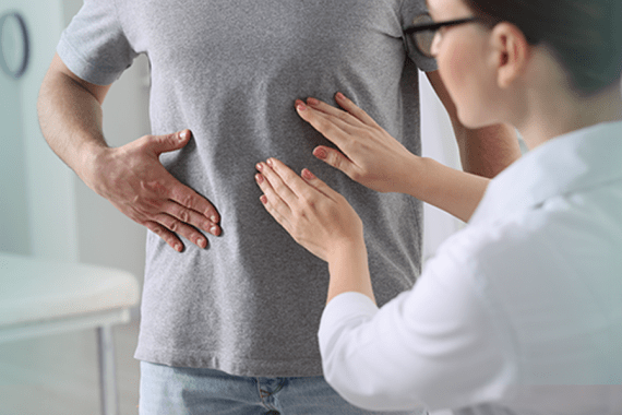 A man is standing in front of a nurse. He has one hand on his stomach. The nurse is touching his stomach with both hands